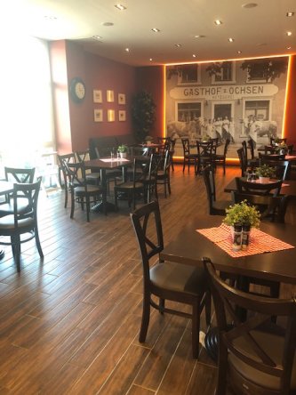 Einladendes Café mit Holzmöbeln, rot-beige Wänden und Schwarz-Weiß-Foto im Hintergrund.