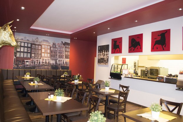 Ein Restaurant mit roten Wänden, Stierbildern und Pflanzen auf Holztischen.