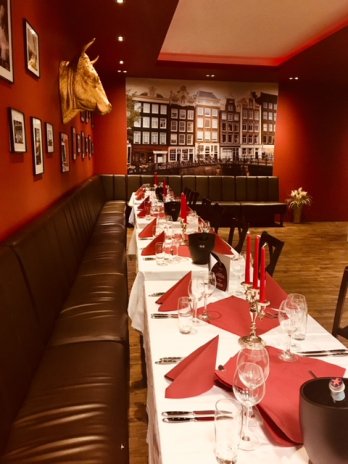 Restaurantinterieur mit langem Tisch, roter Deko, Stierkopf an der Wand und Amsterdam-Bild.