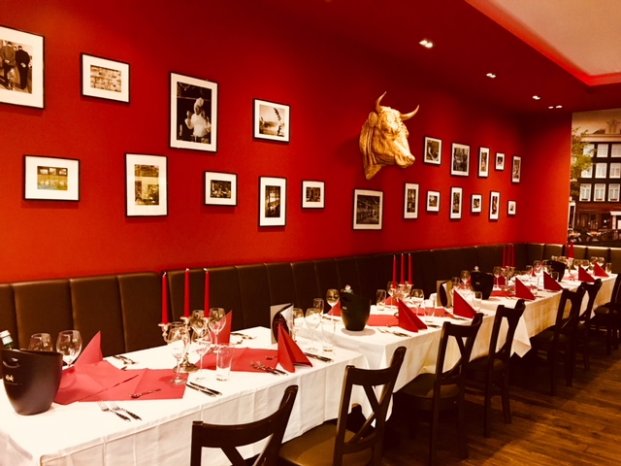Ein Restaurant mit roten Wänden, Bildern und Stierkopf, gedeckte Tische mit roten Servietten.
