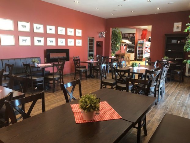Ein leeres Bistro mit Holztischen, roten Wänden und Pflanzen; keine Personen anwesend.