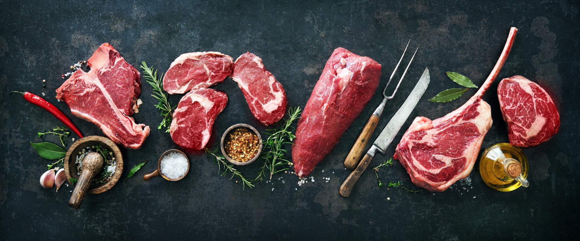 Variety of raw beef meat steaks for grilling with seasoning and utensils